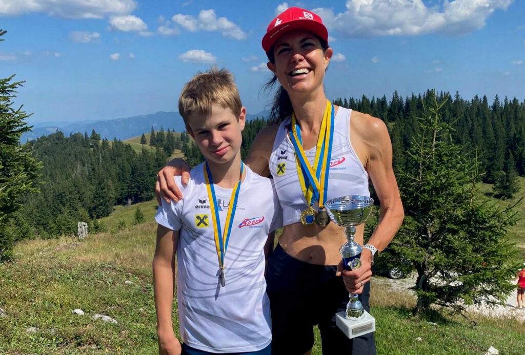 Frau mit Baseballcap hält Pokal in der Hand und umarmt ihren Sohn mit der anderen Hand